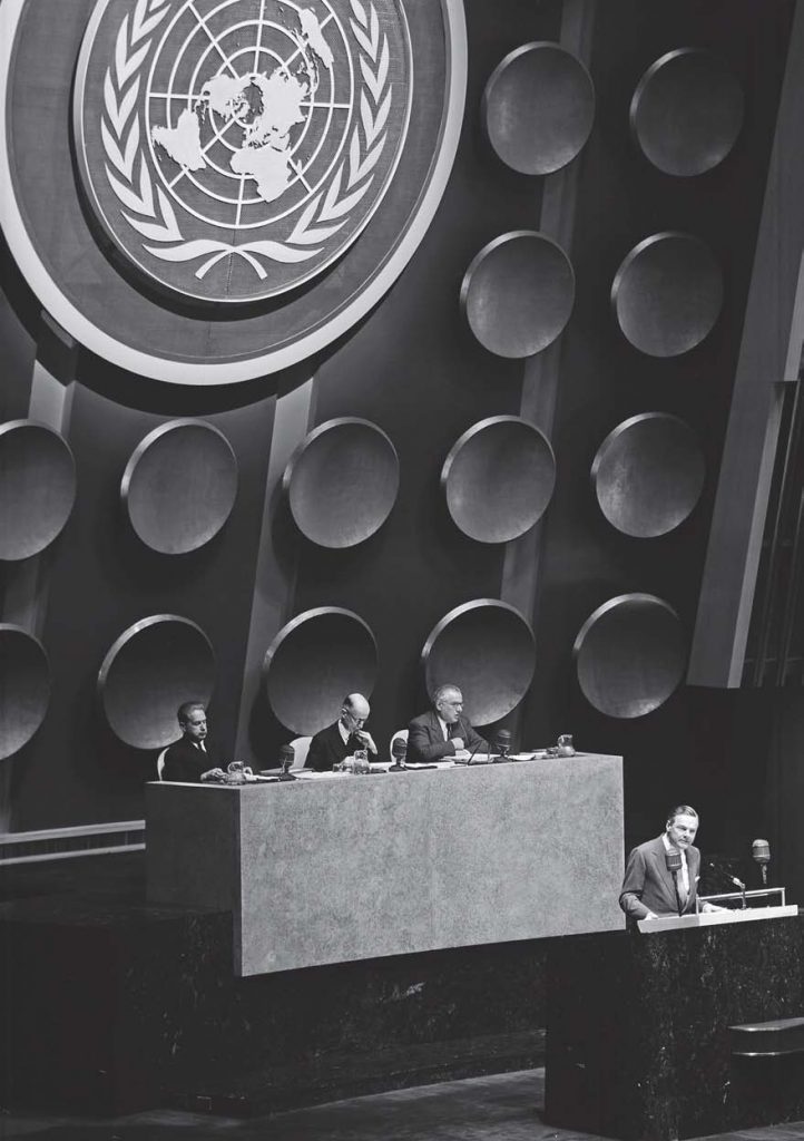 IMMMERSED IN HIS WORLD, DAG HAMMARSKJÖLD SITS FAR LEFT AT THE HIGH PODIUM DURING A MEETING OF THE UN GENERAL ASSEMBLY, NOVEMBER 1954. (UN PHOTO)